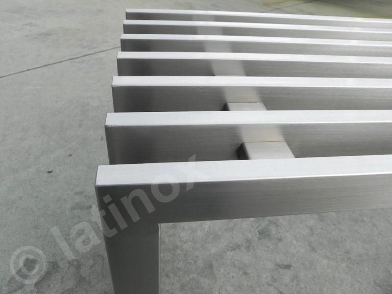 Panca in acciaio inox con doghe orizzontali su una superficie in cemento.