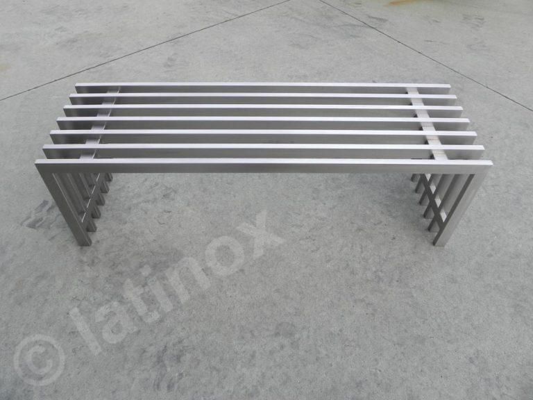 Panca in metallo con doghe orizzontali e supporti verticali, appoggiata su una superficie in cemento.