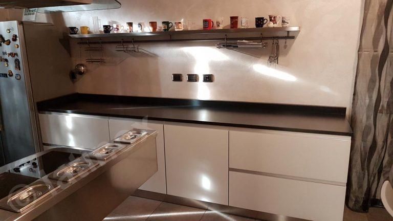 Moderna cucina bianca con ripiani neri, elettrodomestici in acciaio inossidabile e mensola con tazze.