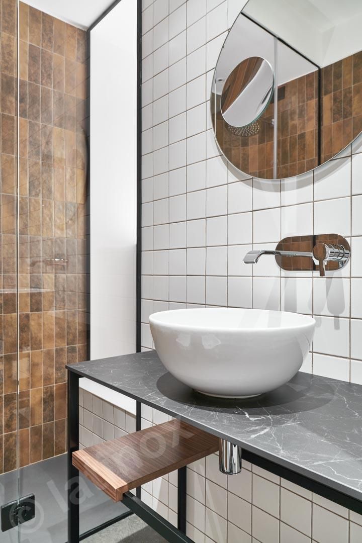 Bagno moderno con lavandino bianco, piano di lavoro scuro e parete piastrellata marrone.