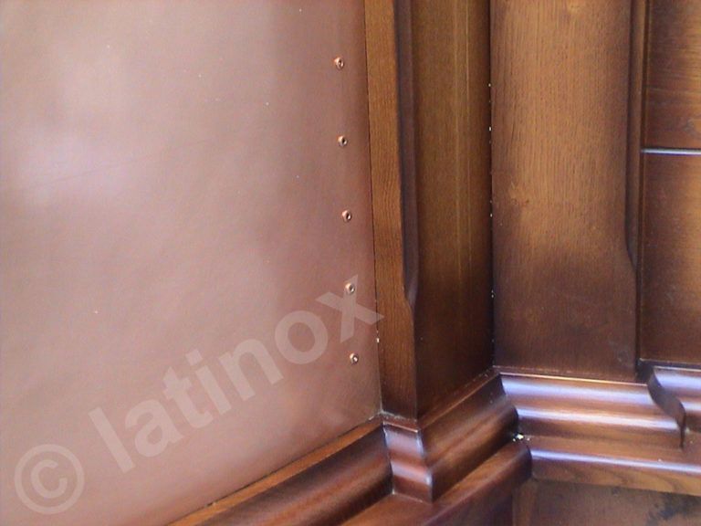 Parete rivestita in rame con rivetti a vista, finiture in legno scuro e dettagli angolari.