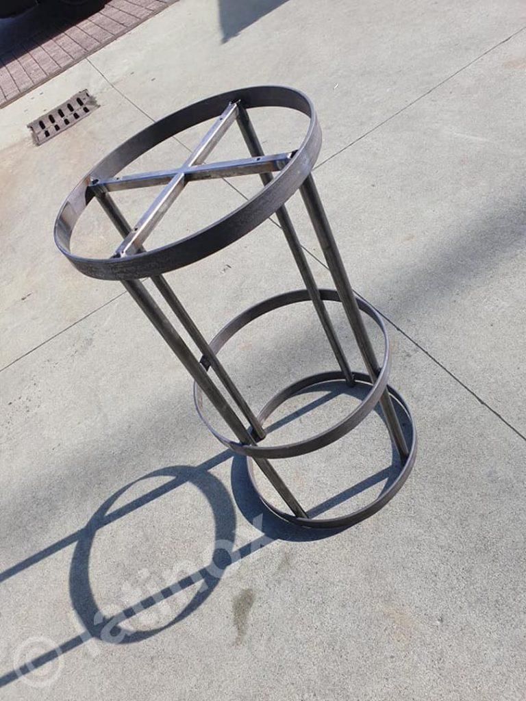 Telaio in metallo saldato per un oggetto a forma di barile, con sezioni superiori e inferiori circolari collegate da barre verticali.