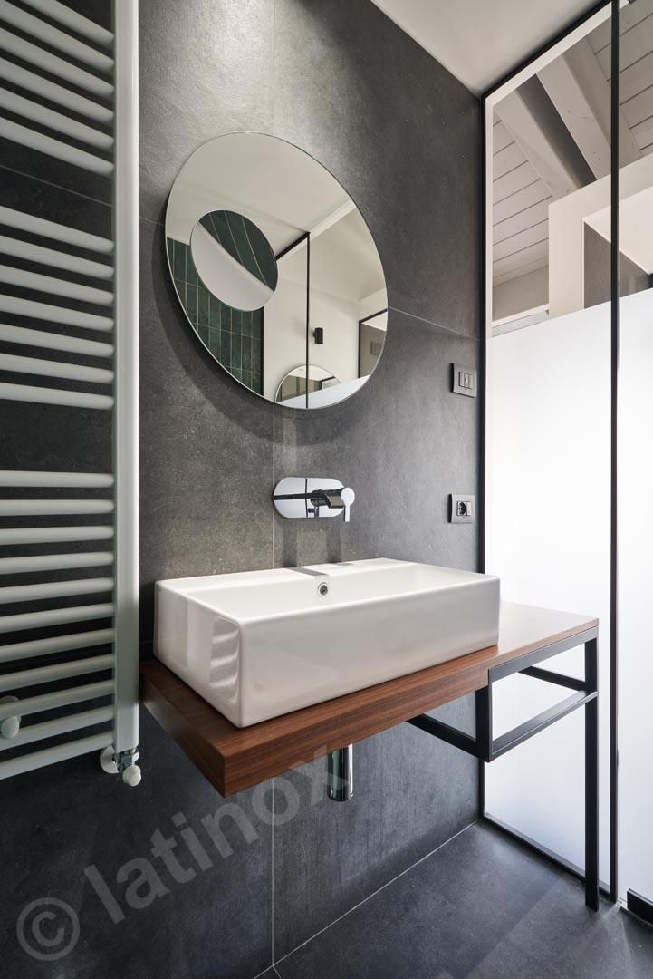 Bagno moderno con lavandino rettangolare, specchio rotondo e scaldasalviette su una parete grigia.