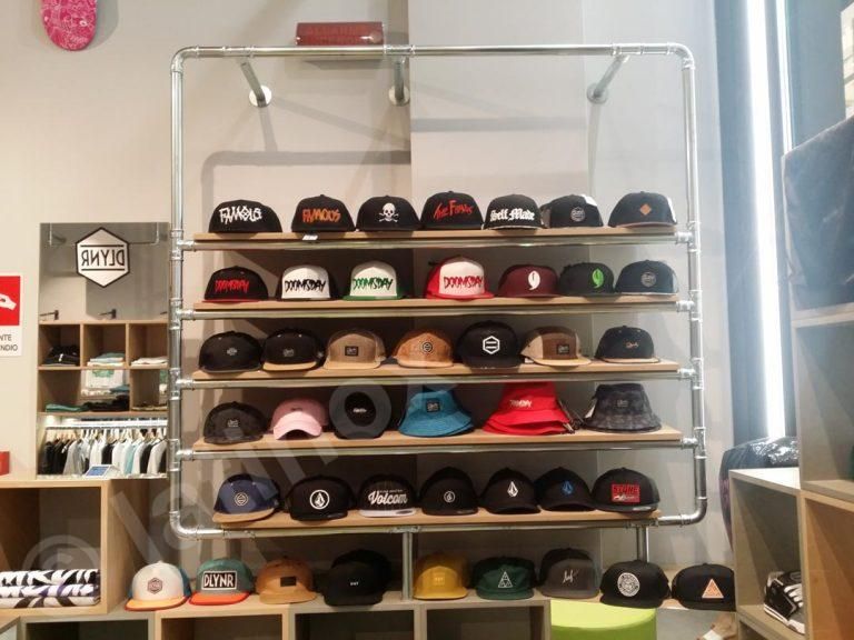 Cappelli esposti su scaffali di legno fissati a una rastrelliera metallica per tubi in un negozio.