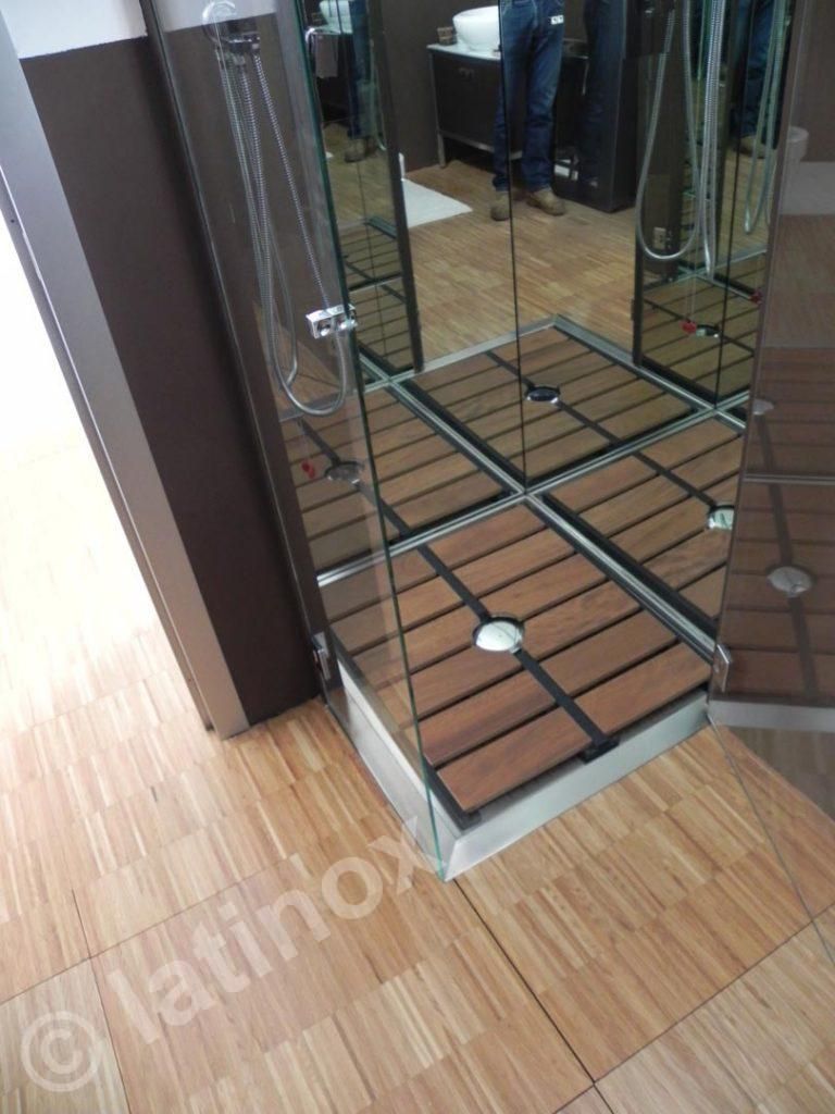 Box doccia con pareti a specchio e pavimento effetto legno, adiacente a un mobiletto marrone, all'interno.