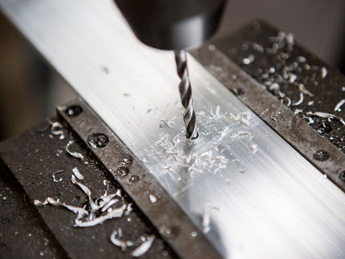 Punta da trapano che pratica un foro in una barra di metallo su una macchina per metalli, producendo trucioli di metallo.