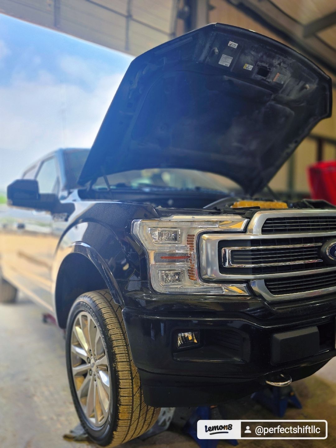 A black ford f150 with the hood open is sitting in a garage.