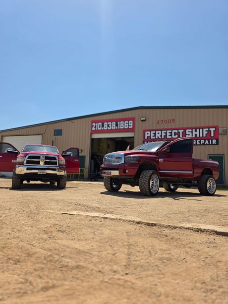 Two red trucks are parked in front of a perfect shift repair shop.
