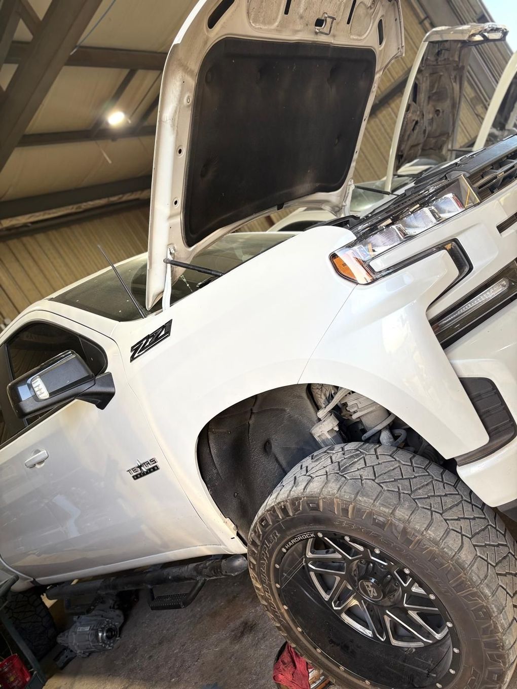 A white truck with the hood up is parked in a garage.