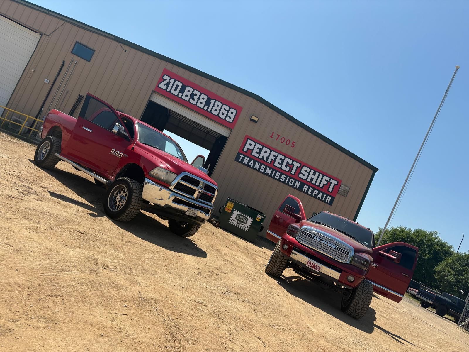 Two red trucks are parked in front of a building that says perfect shift transmission service.