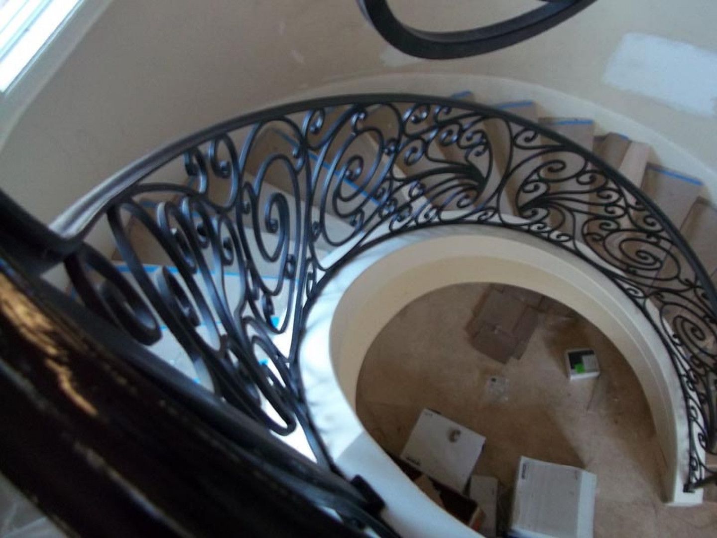 A high-angle view of a curved staircase with an ornate, black wrought-iron railing overlooking a circular foyer area.