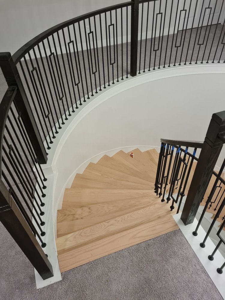 A curved wooden staircase with dark metal railings and spindles, descending from a carpeted landing.