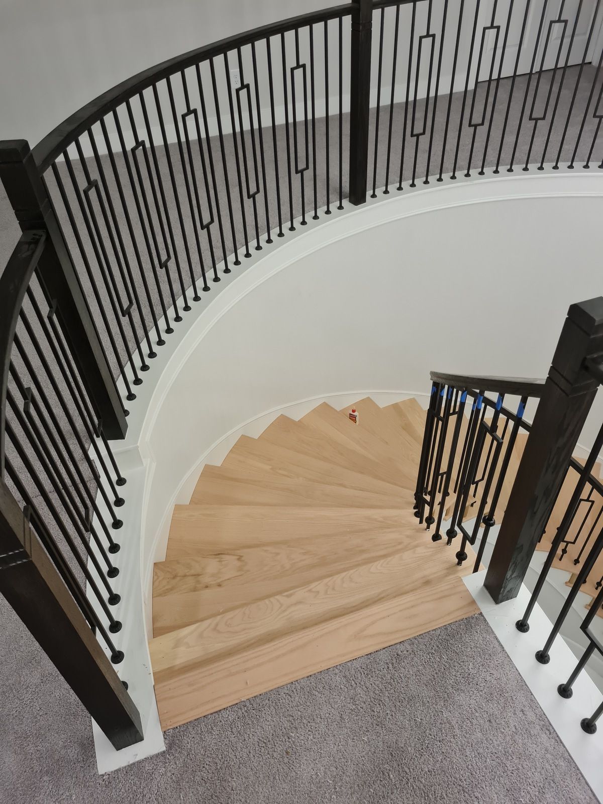 A curved staircase with wooden treads, black metal railings, and grey carpet on the landing.