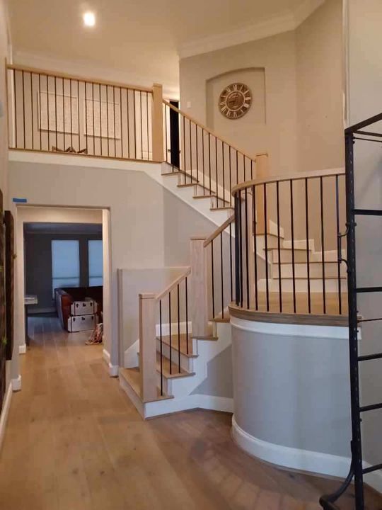 A foyer with light wood floors, beige walls, and a curved staircase featuring black metal railings and wood handrails.