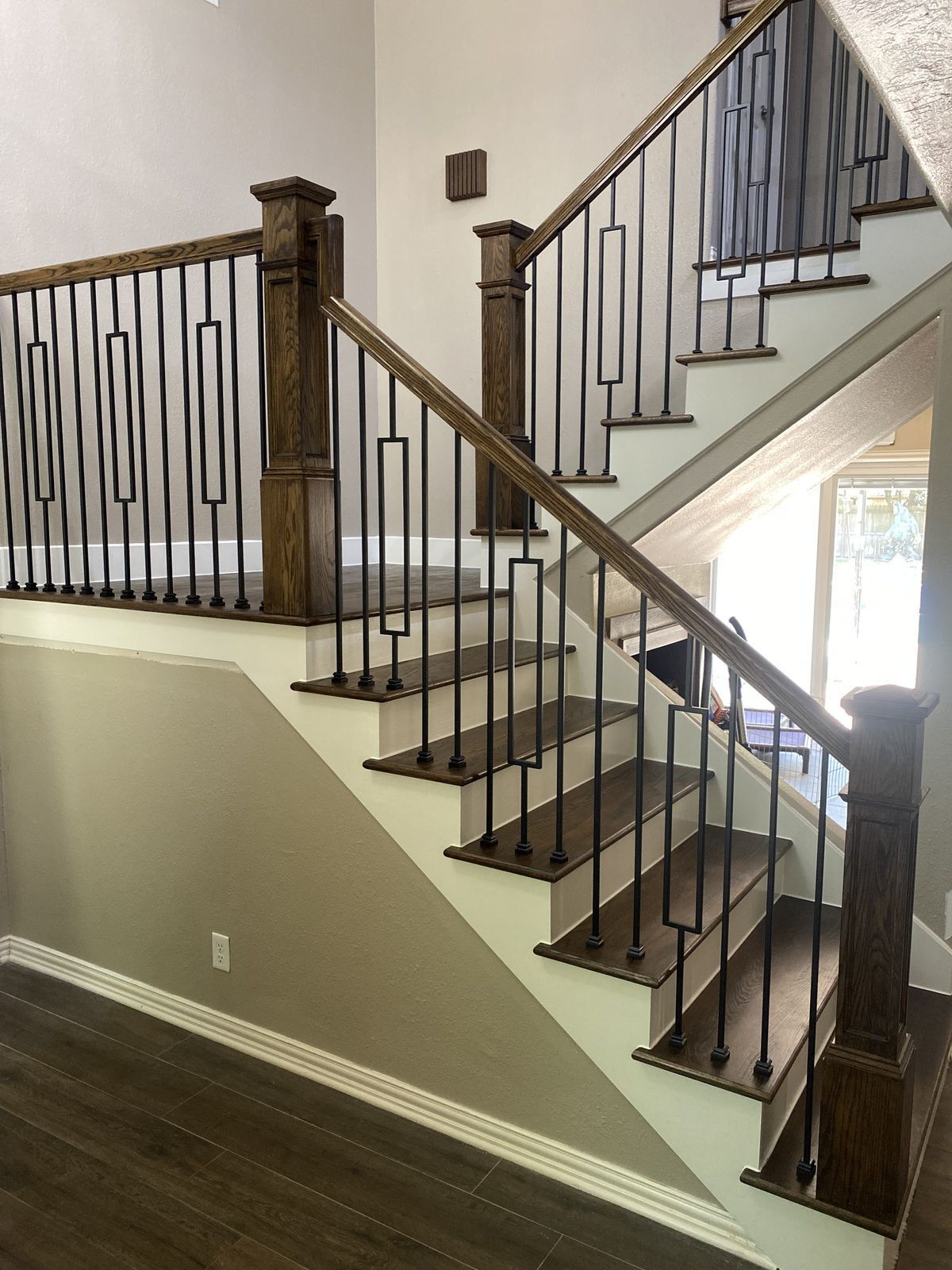 A staircase with dark wood treads and a white stringer, featuring a wooden handrail and black metal balusters.