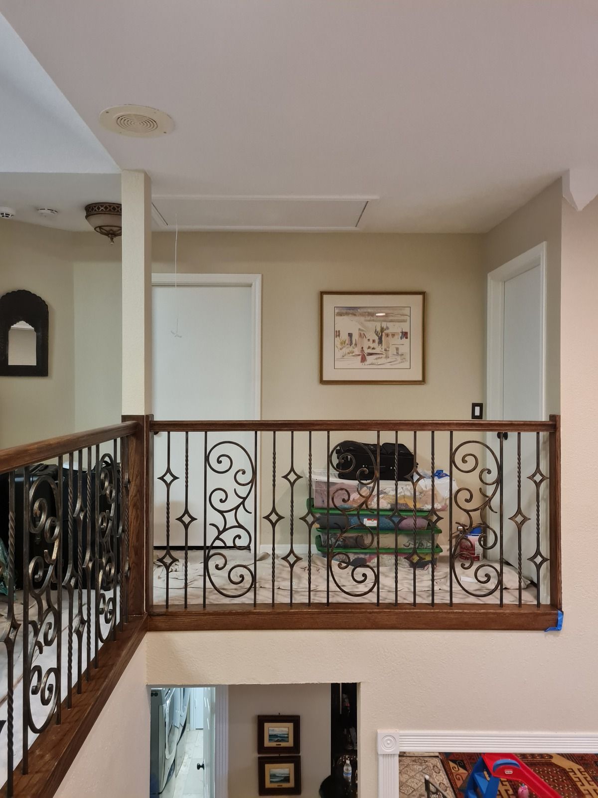 A hallway view of an interior staircase railing with ornate black metal spindles and a wood handrail.
