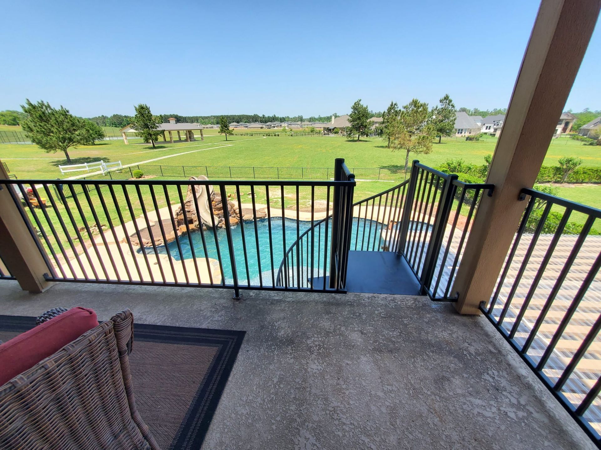 A balcony overlook with a black railing, showing a view of a backyard swimming pool and open green landscape.