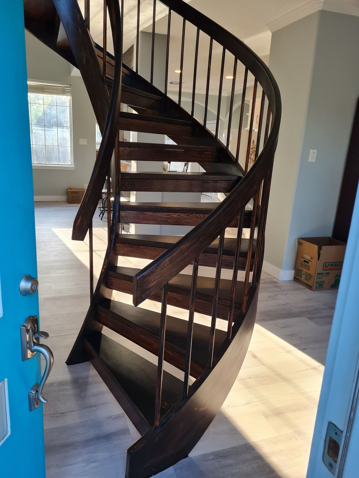 A dark wood spiral staircase set in a modern home entry, viewed through an open blue door.