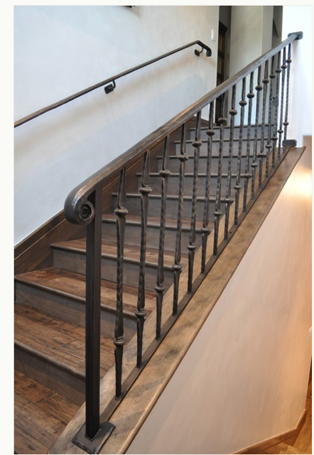 A staircase with dark wood steps, a wooden handrail, and black metal balusters with decorative twisted-metal details.