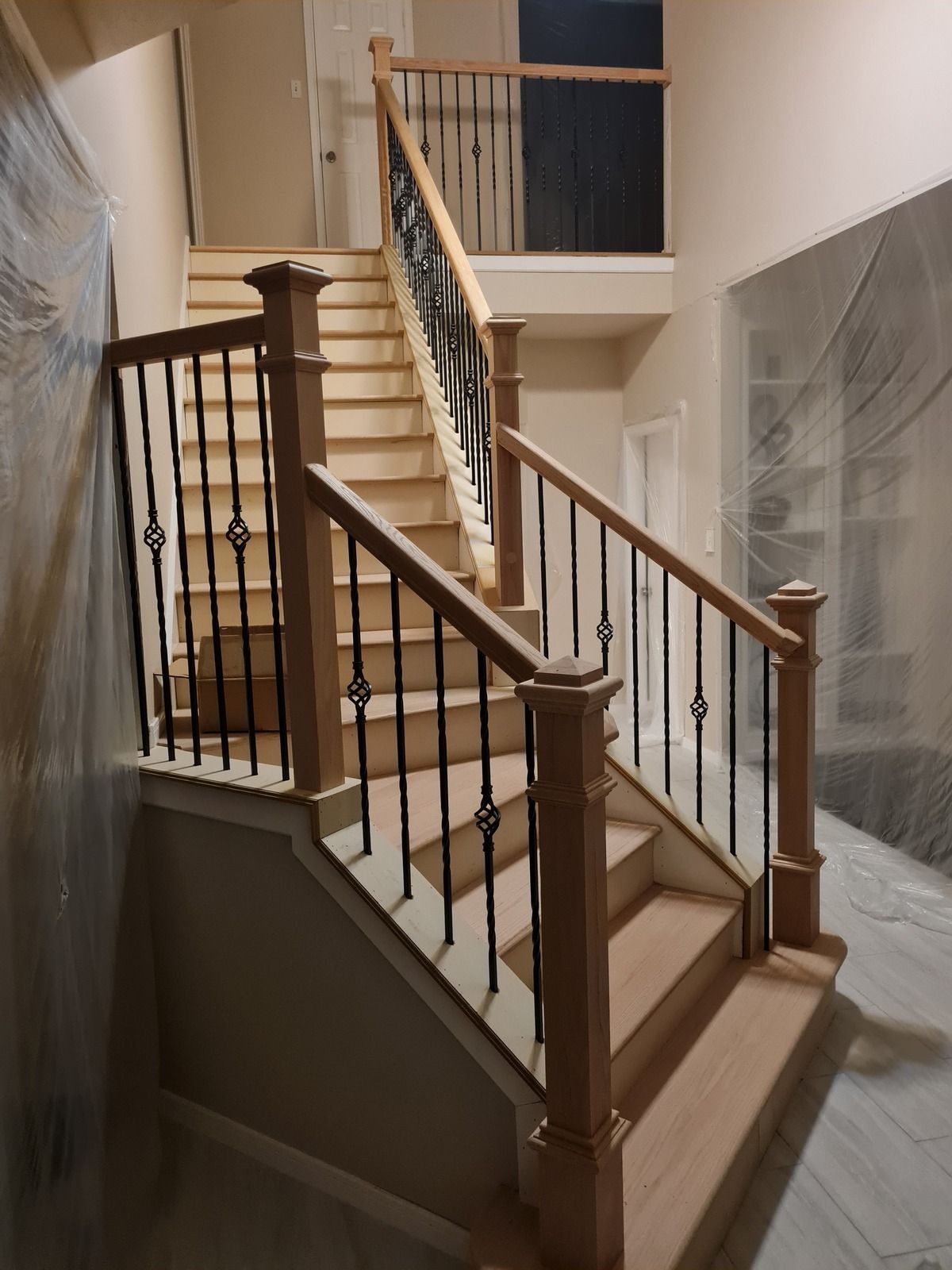 A wooden staircase with black iron spindles, wood railings, and square posts in a foyer.