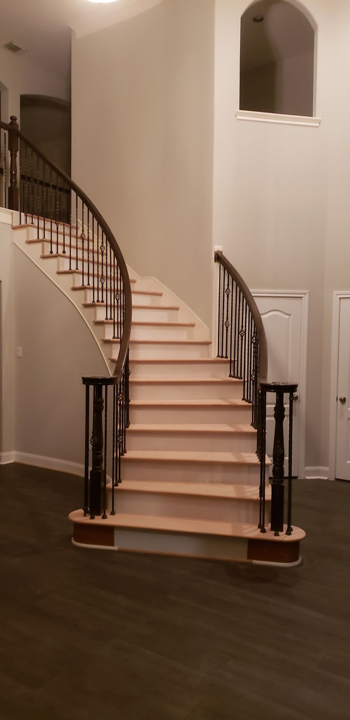 A curved wooden staircase with dark metal railings ascends from a foyer with dark wood flooring to an upper landing.