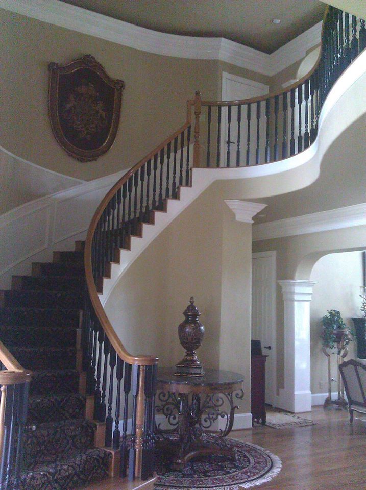 A curved staircase with wooden railings and dark carpet in an entryway, featuring a decorative wall plaque and table.