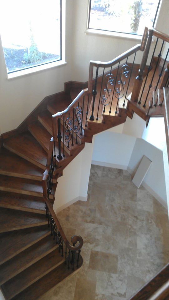A winding wooden staircase with ornate dark metal railings curves down toward a tiled foyer in a bright, modern home.