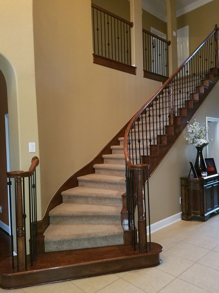A grand staircase with wood railings and carpeted stairs in a beige, tiled entryway with a small table and decor.