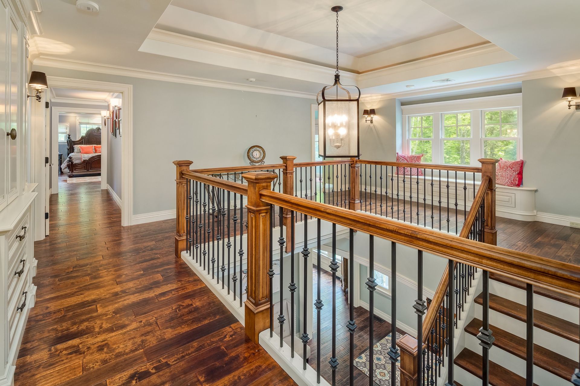 A hallway overlooks a staircase with wooden railings and metal spindles, featuring hardwood floors and a pendant light.
