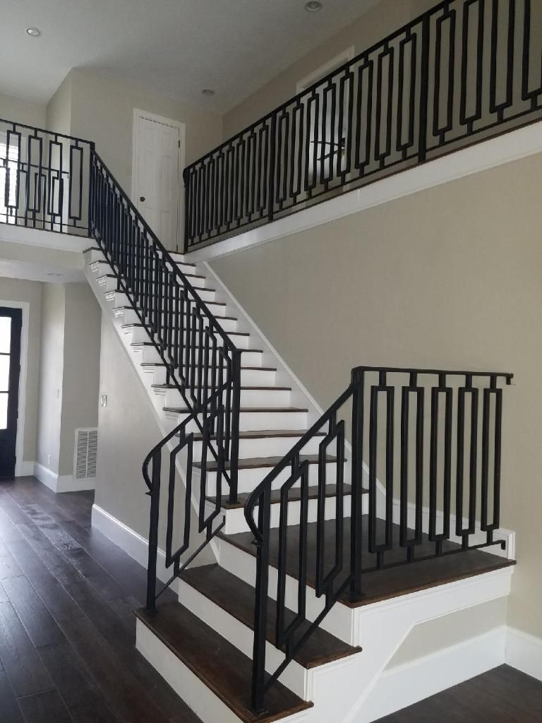 A modern staircase with dark wood treads, white risers, and a distinct black metal railing with a geometric pattern.