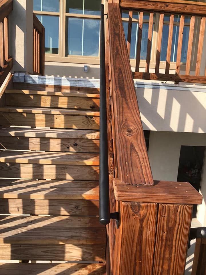 A black handrail mounted on a brown wooden staircase leading up to a deck area under bright sunlight.