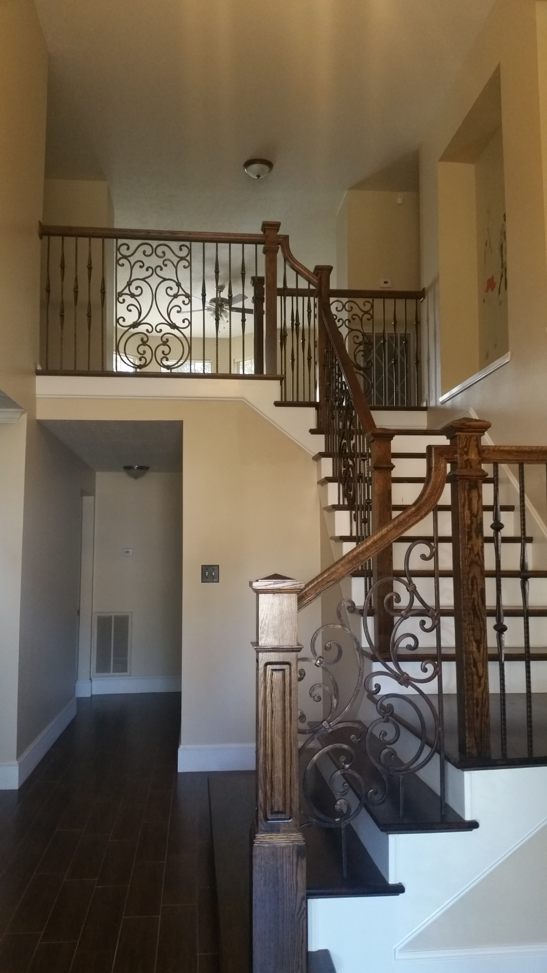 An interior view of a home with a wooden staircase, ornate iron railings, and dark hardwood flooring.