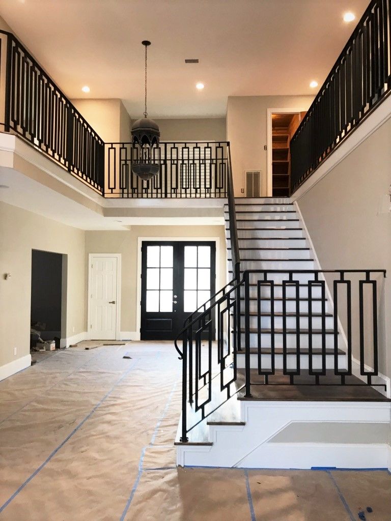 A bright home entryway with a central staircase featuring black geometric railings, light wood floors, and double doors.