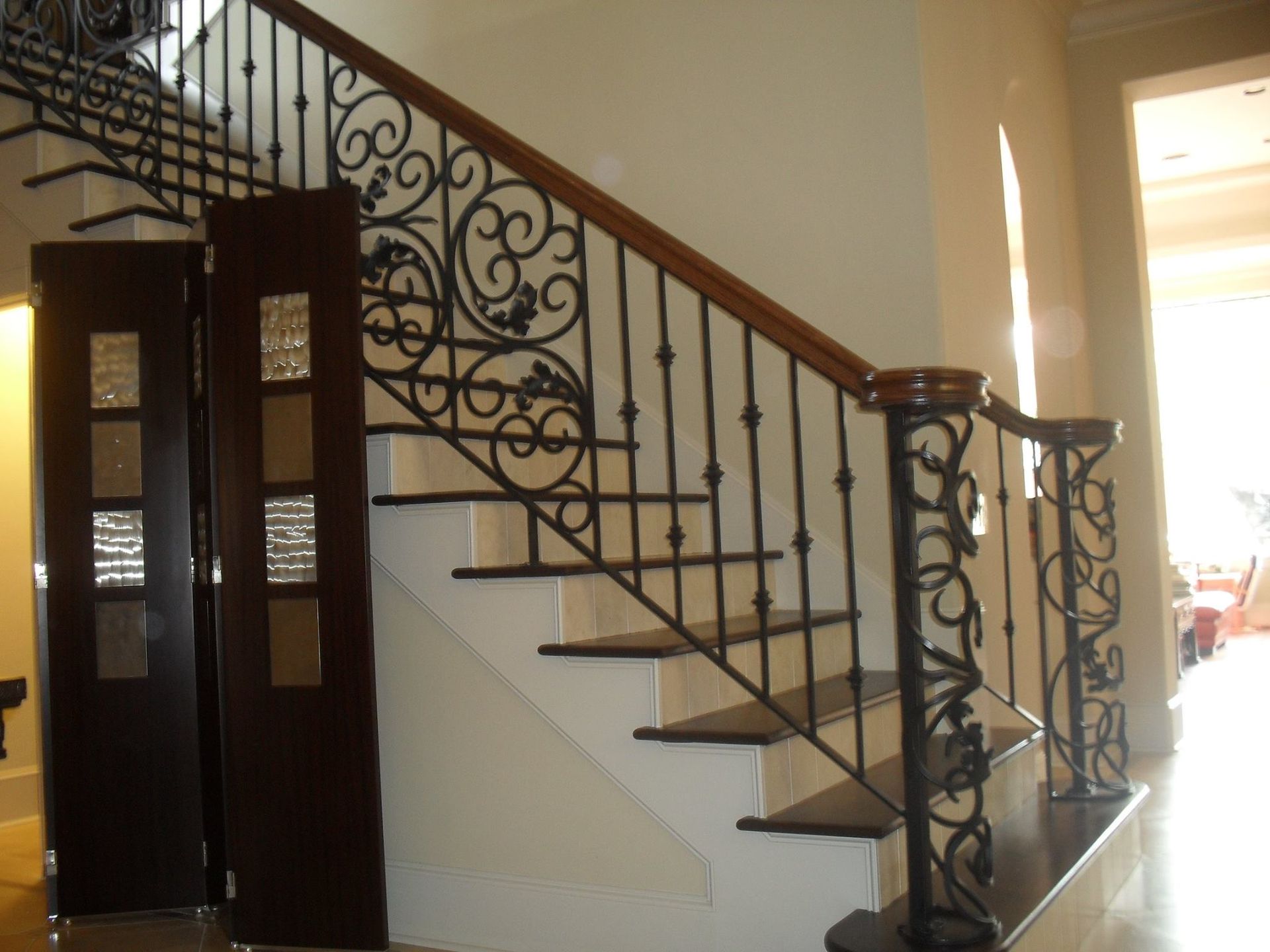 Interior staircase with dark wood steps, a wooden handrail, and intricate black wrought iron railings and posts.
