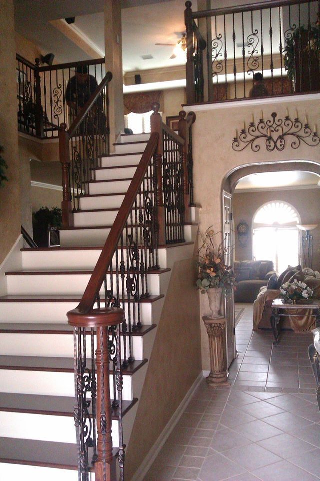 A staircase with dark wood railings and black iron balusters leads to an upper level next to an arched entryway.