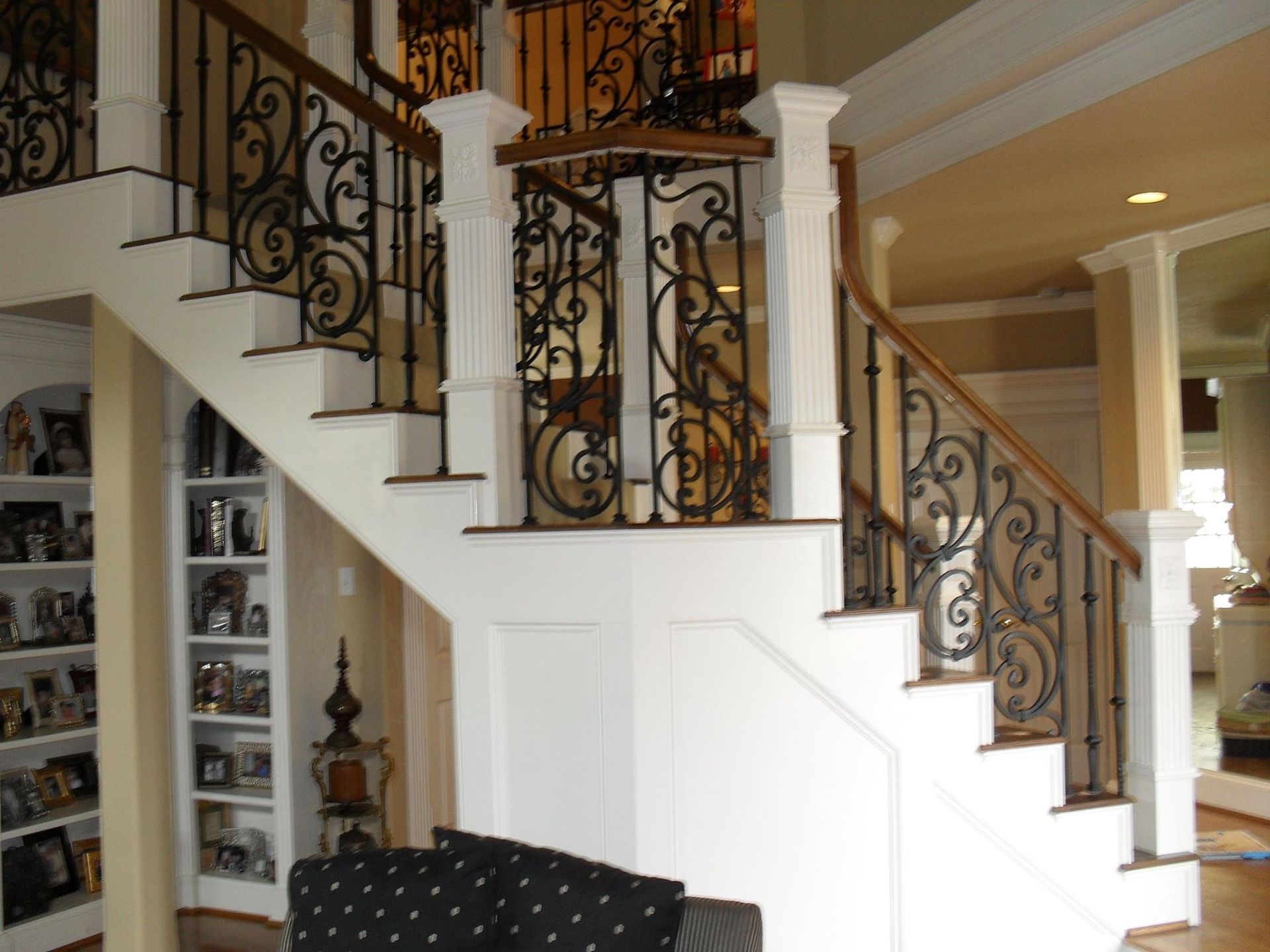 A grand staircase with white wood paneling, dark wrought iron railings, and wooden handrails in a home interior.