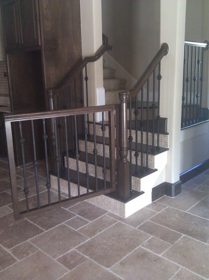 A dark wood baby gate installed at the base of a carpeted staircase with dark wood railings and metal balusters.