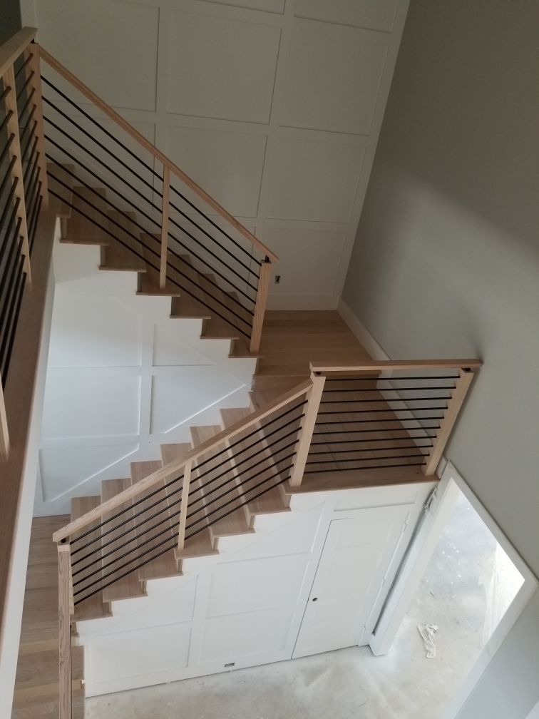 A modern staircase with light wood treads, metal horizontal railings, and white paneled walls enclosing the space below.