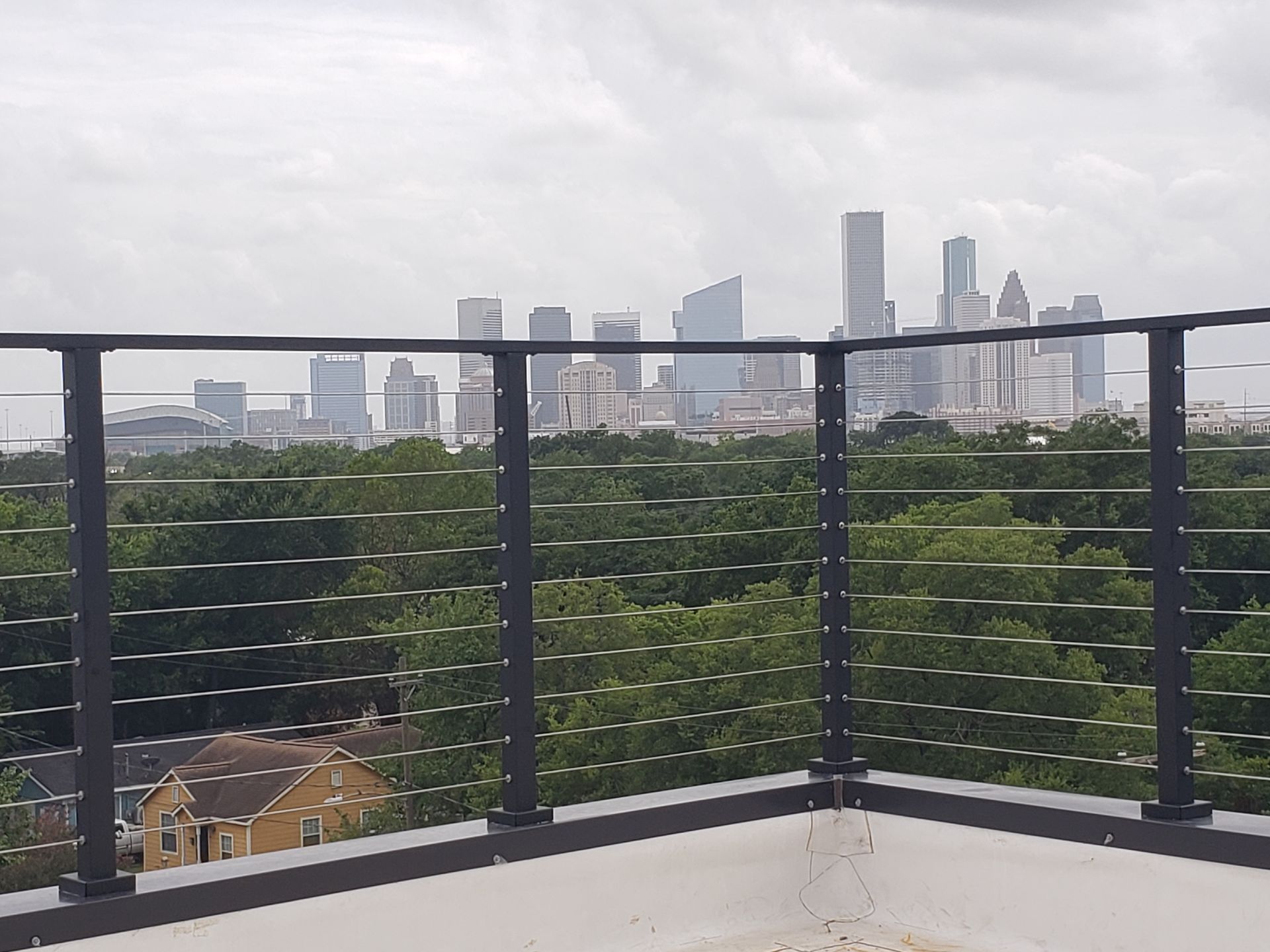 A view of a city skyline over a lush green forest, seen from a balcony with a modern black railing.