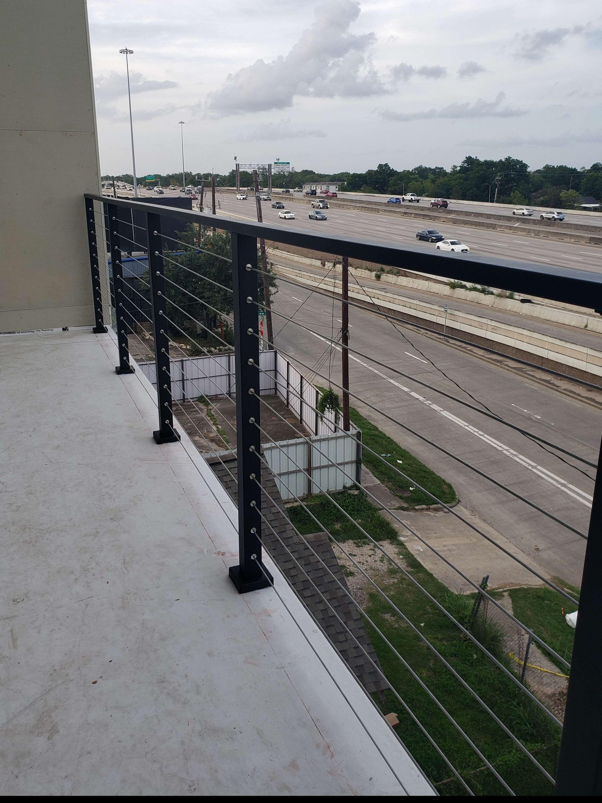 A black metal railing with horizontal cable infill on a balcony overlooking a multi-lane highway.