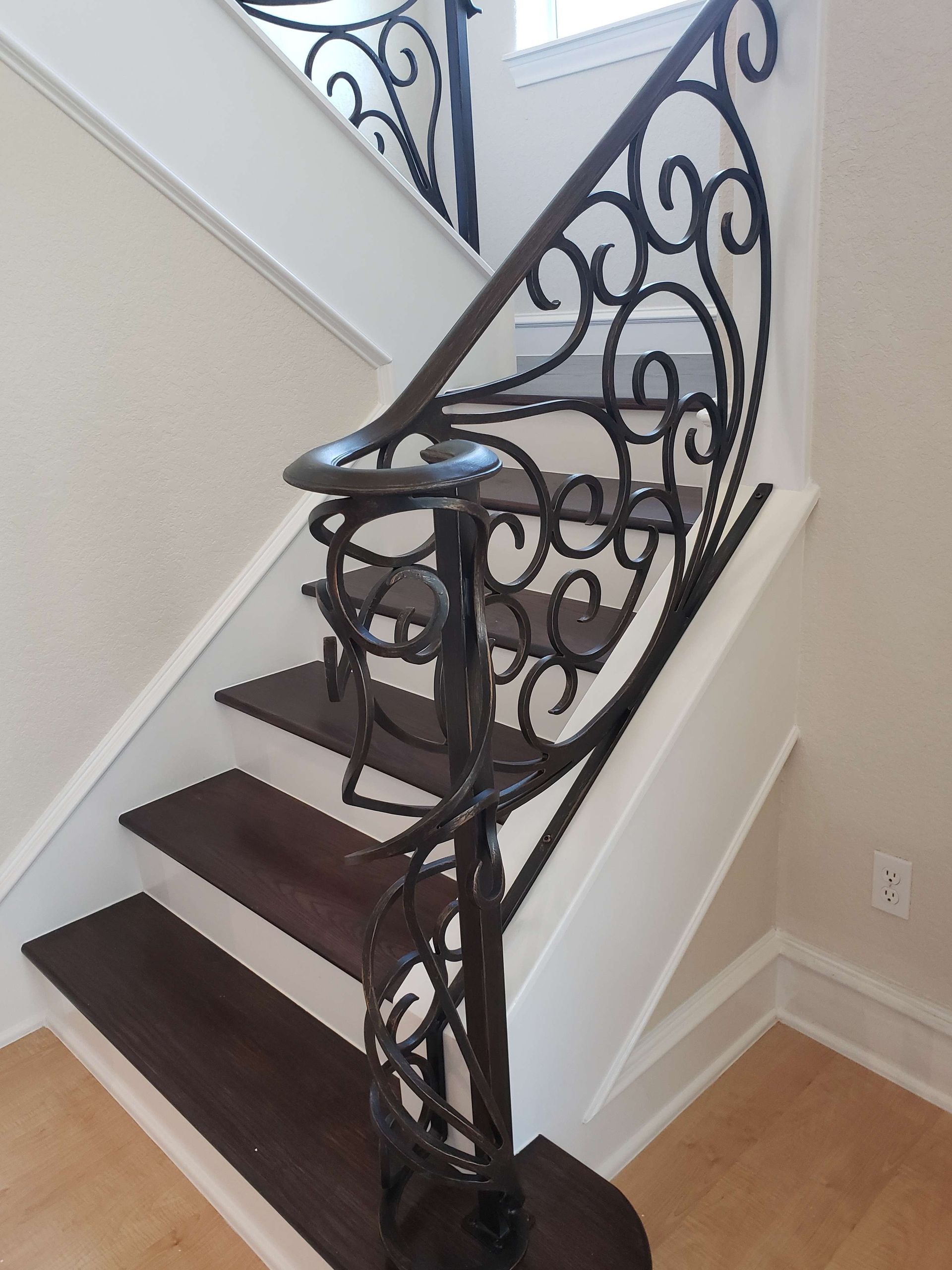 An indoor staircase with dark wood treads, white risers, and an ornate, black wrought-iron handrail featuring scrollwork.