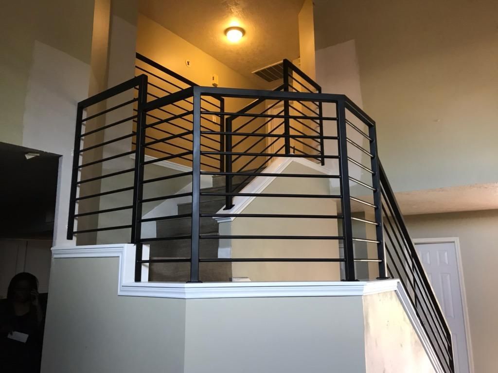 Black horizontal metal railings installed along an indoor staircase and landing area in a neutrally painted home.