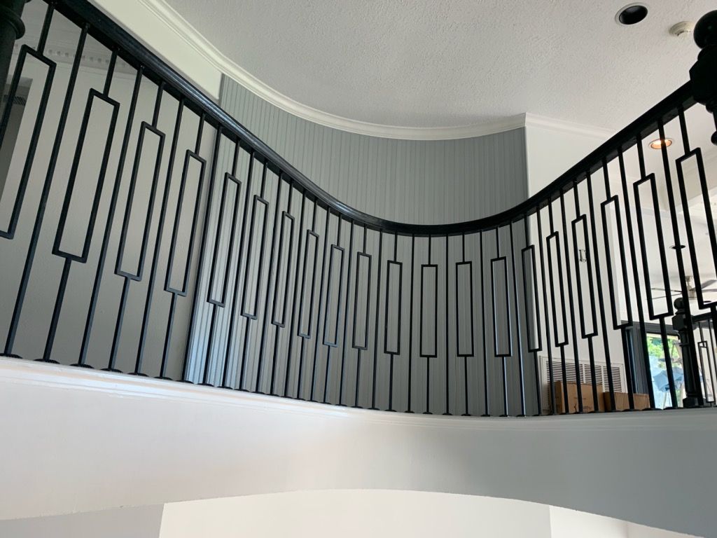 A curved staircase railing with black metal balusters in a modern, light-filled interior.