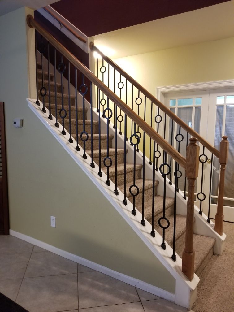 A staircase with beige carpet, a wooden handrail, and black metal balusters with ring details, set against a yellow wall.