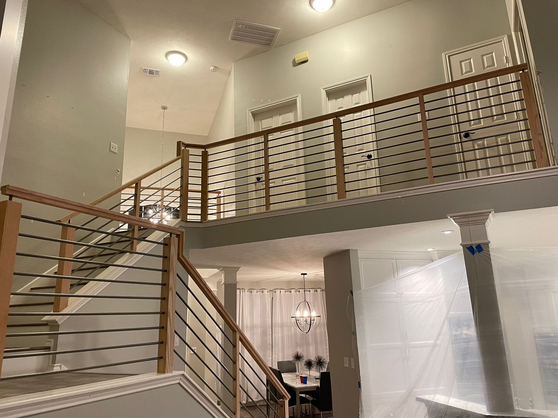 A bright entryway featuring a staircase with a wooden and cable railing, leading to a second-floor landing with two doors.