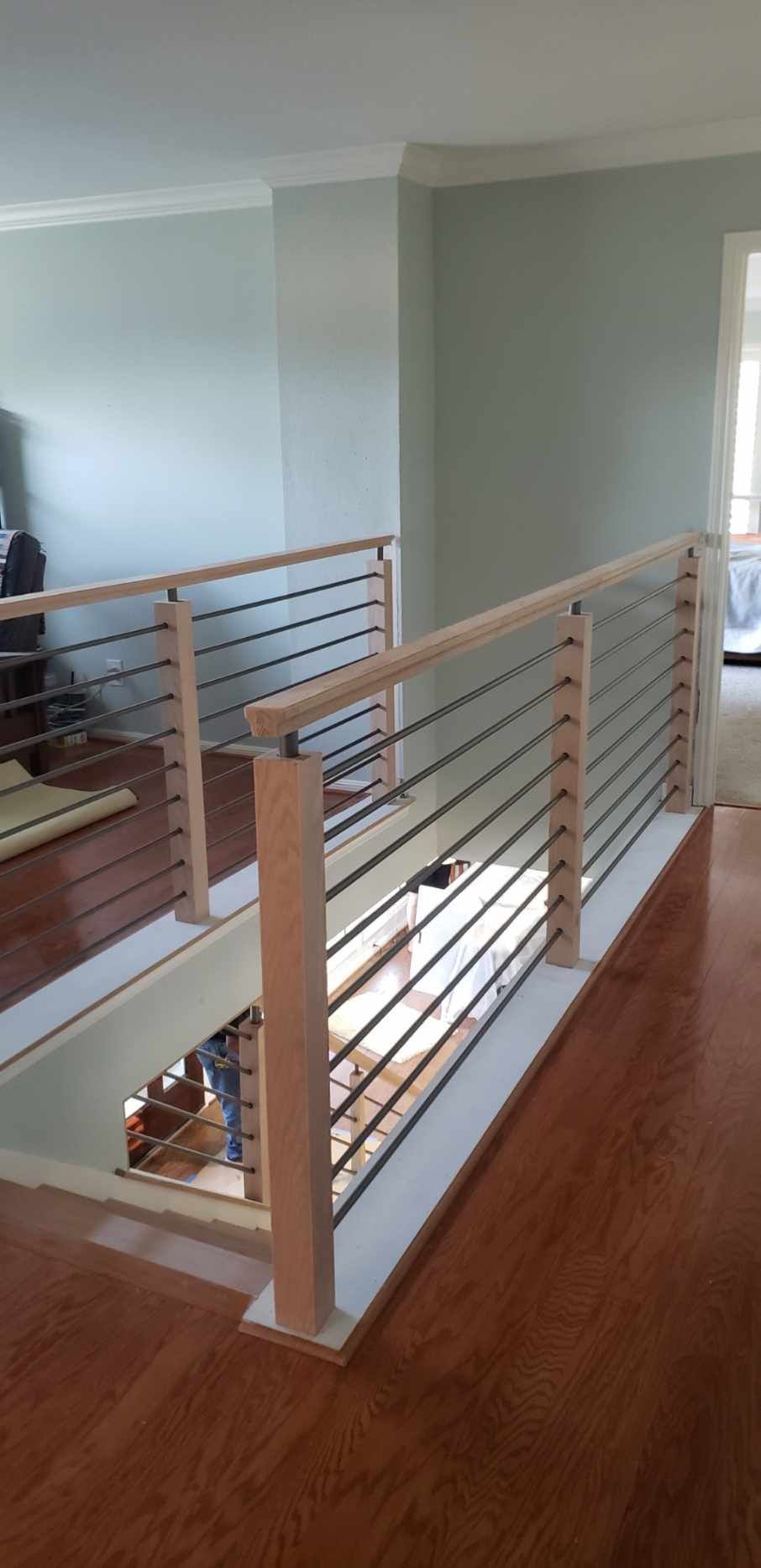 A wooden railing with horizontal metal cables lines the edge of a staircase landing in a bright, modern indoor space.