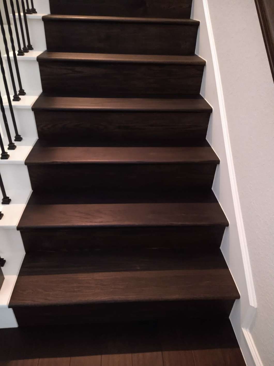 A staircase featuring dark wood treads and white risers with black metal balusters along the left side.