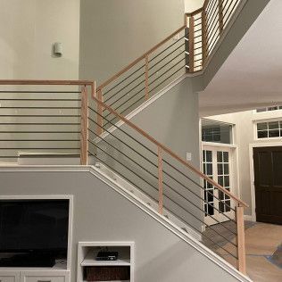 A wooden staircase with metal horizontal railings, light gray walls, and an entryway with a dark door in the background.