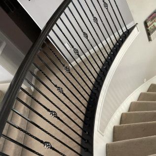 A curved staircase with black metal balusters featuring decorative knots, leading upstairs with carpeted steps.