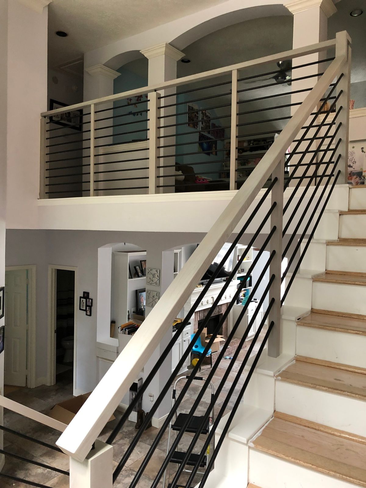 Indoor staircase with wooden steps and a white railing featuring horizontal black metal bars leading to an upper landing.